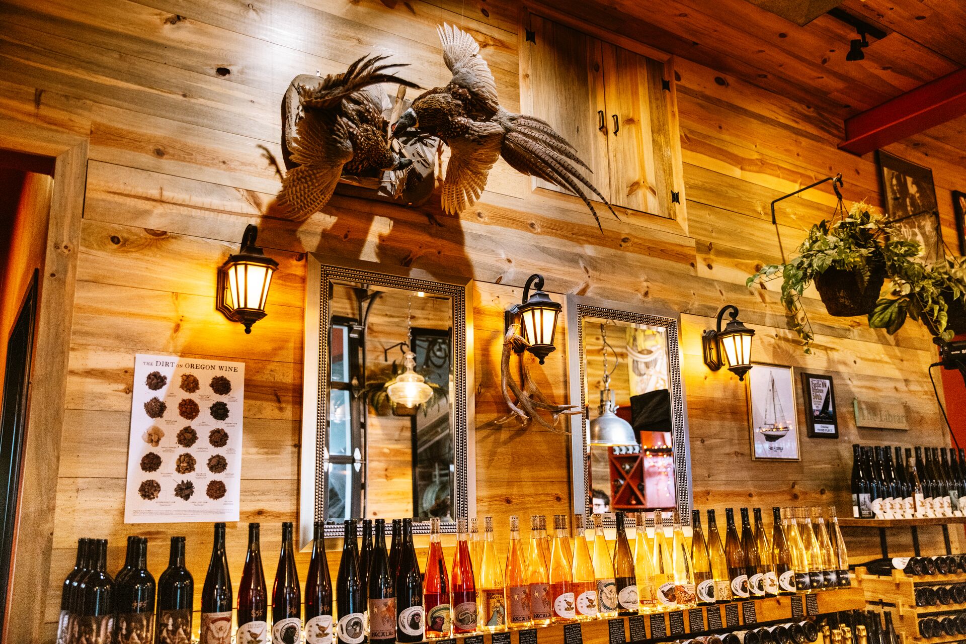 Bottles of wine lined up beneath lanterns and mirrors on the tasting room's wood-paneled wall